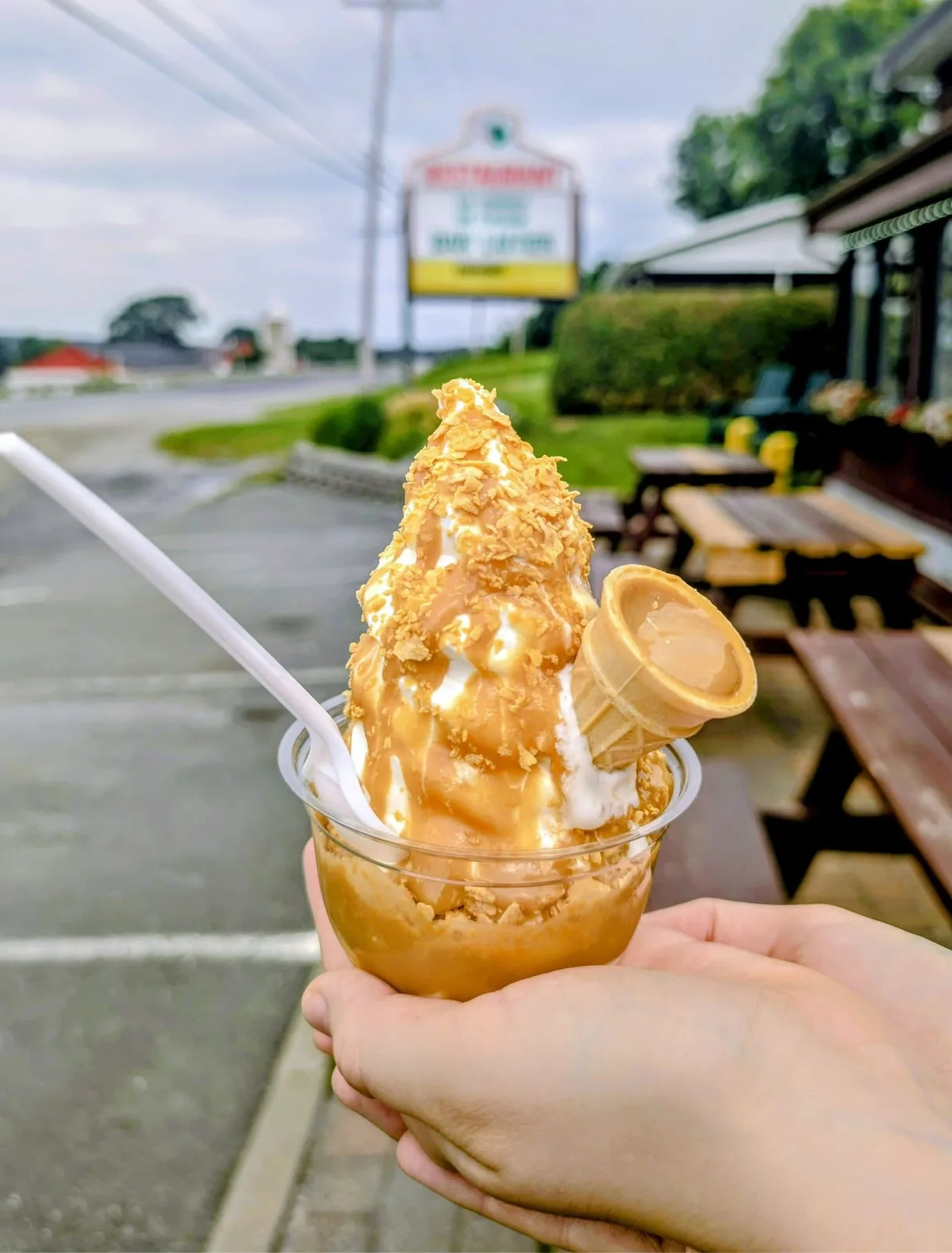 Coupe de crème glacée molle nappée de coulis d'érable et de flocons croquants, avec un petit cornet planté dessus, tenue devant le restaurant