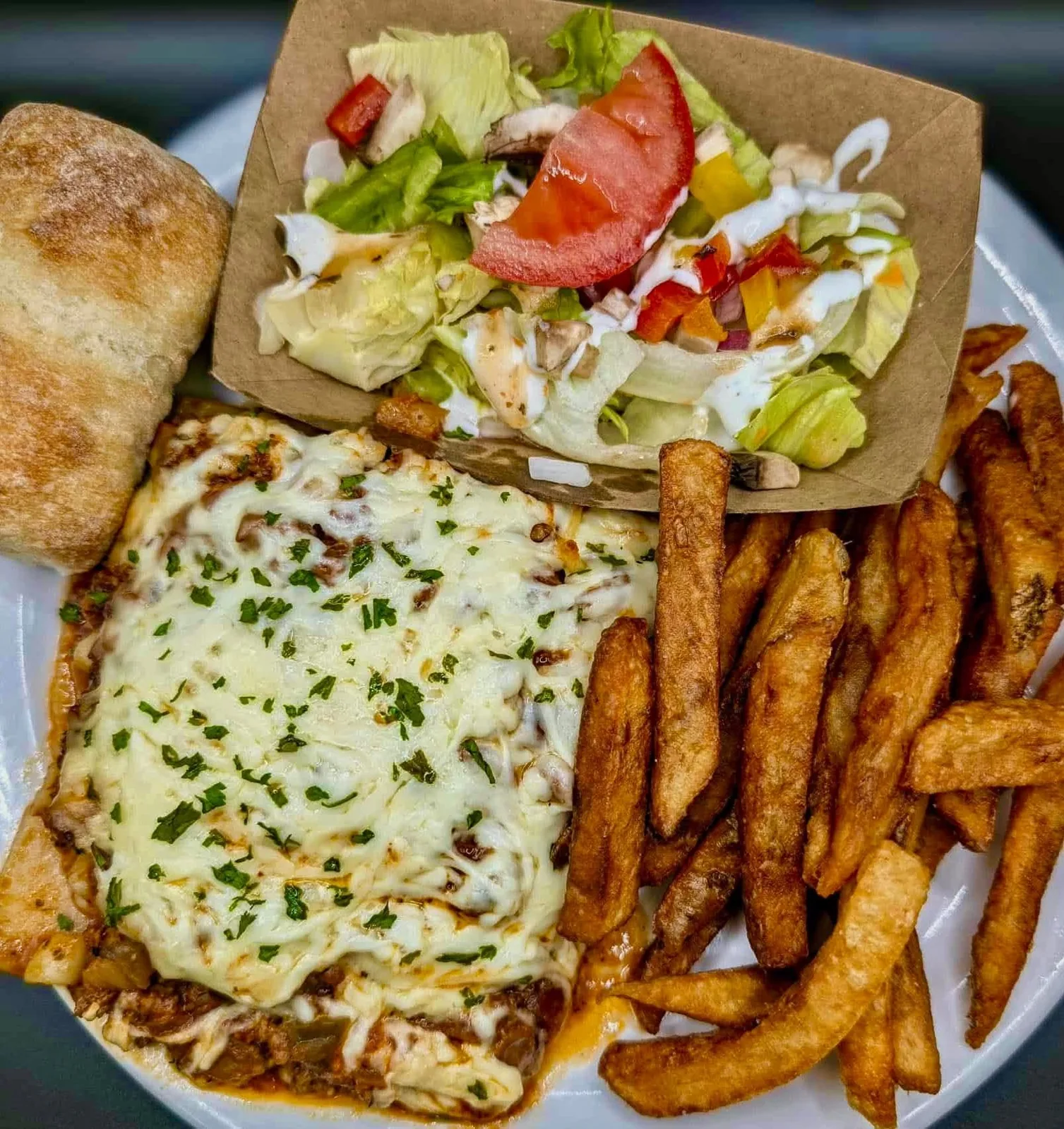 Assiette gratinée au fromage fondu servie avec frites maison, pain et salade