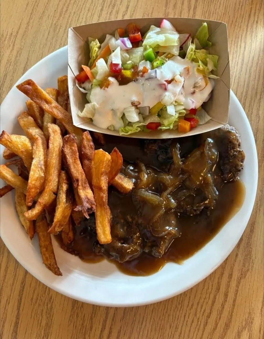 Steak haché nappé de sauce aux oignons avec frites maison et salade